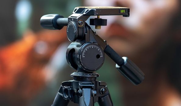 Large black professional tripod with swivel head on a busy street