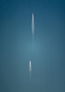 Two planes with long white condensation trails behind them high in the blue sky.