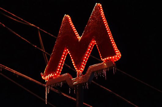Sign M at the entrance to one of the Moscow metro stations, covered with ice and icicles, during freezing rain.