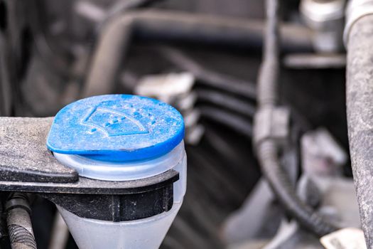 A close-up side view of a blue plastic cap covering a tube for filling a windshield wiper fluid tank.