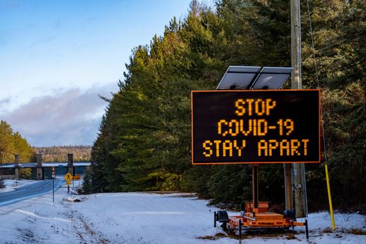 Algonquin Provincial Park, Ontario, Canada - November 28, 2020: A portable electronic message board trailer at the East Gate to Algonquin Provincial Park reads "STOP COVID-19, STAY APART".