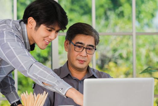 Asian senior and junior two businessmen discuss something during their meeting consultation project, Mature boss with a business partner working together on the laptop computer on desk home office