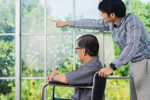 Asian senior disabled businessman in wheelchair discuss interacting together with the team in the office. The old man in a wheelchair and his young son talking to and comforting bound father