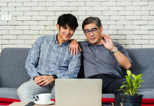 Asian senior businessman with laptop computer discuss together with young team in office. Father man and his son sit on sofa talking chatting on video call conference on laptop in living room at home
