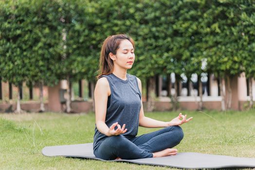 Asian young woman doing yoga outdoors in meditate lotus pose sitting on green grass with closed eyes at the garden park, health care concept