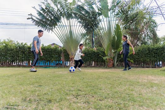 Asian young mother, father and child daughter playing soccer outside in nature a field garden park. Happy family kid funny play football together in summer, sport and exercises for healthy lifestyle