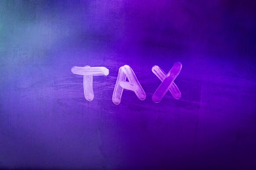 word tax hadwritten on night wet window glass surface with purple color in blurry background