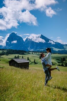 Alpe di Siusi - Seiser Alm with Sassolungo - Langkofel mountain group in background at sunset. Yellow spring flowers and wooden chalets in Dolomites, Trentino Alto Adige, South Tyrol, Italy, Europe. Summer weather with dark clouds rain, couple men and woman on vacation in the Dolomites Italy