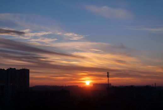 Sunset of the red sun among the clouds over the city.