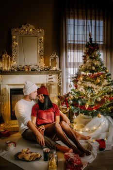 Cute, young couple by fireplace with a Christmas tree,Family sitting on a floor. Couple near christmas tree with candle lights