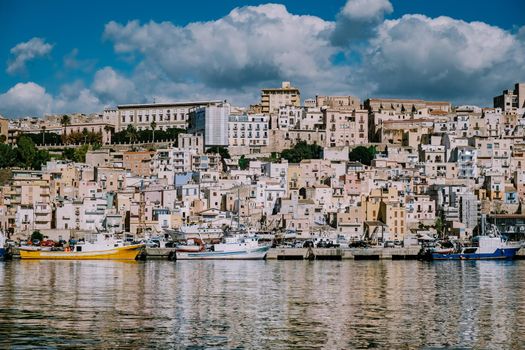 Sciacca Sicily October 2020, fishing boats and people repair nets at the colorful city of Sciacca overlooking its harbour. Province of Agrigento, Sicily. High quality photo