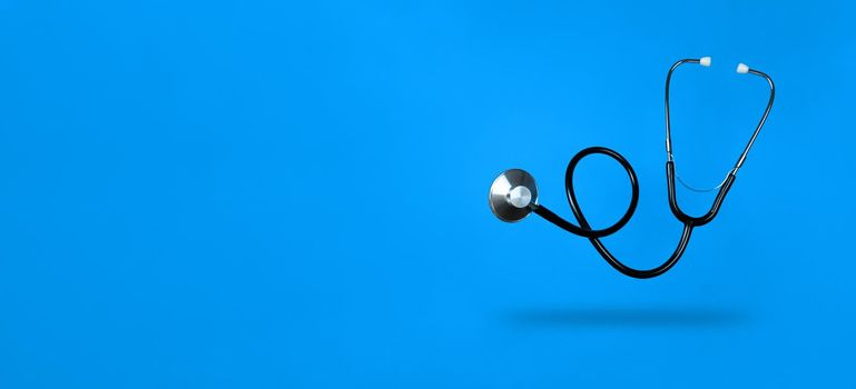 Levitating stethoscope on blue background and shadow under it with copy space. Stock photography.