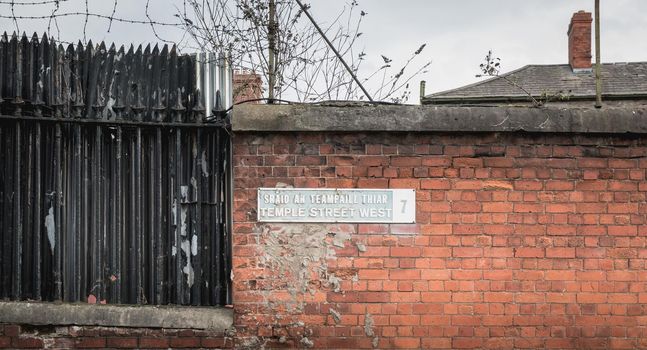 Temple Street West 7 written in English and Irish on a metal plaque on a red brick mir