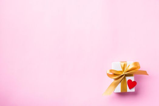 Valentines' day background concept. White gift box with a golden bow ribbon and wood red hearts composition greeting card for happy love isolated on pink background with copy space. View from above