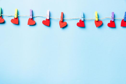 Valentine's day concept. red heart-shaped valentines decoration hanging with wood clips for happy love on the rope greeting card isolated on blue background with copy space