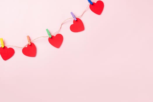 Happy Valentine's day background. red heart shaped valentines decoration hanging with paper clips on the rope for love composition greeting card isolated on pink background with copy space