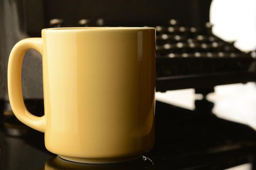 A closeup of a writers desktop with a shallow depth of field focus on the coffee cup with area for copyspace and a blurry typewriter in the background.