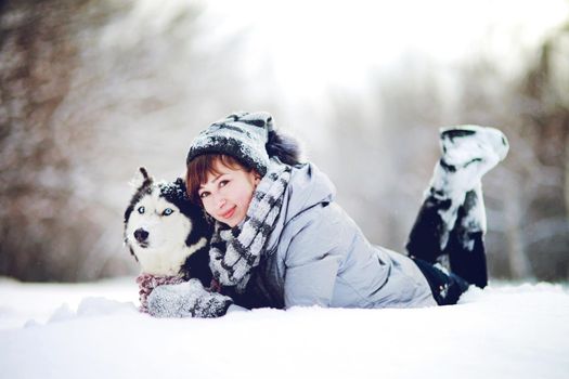The Girl lies in the snow with a siberian husky dog in the winter forest