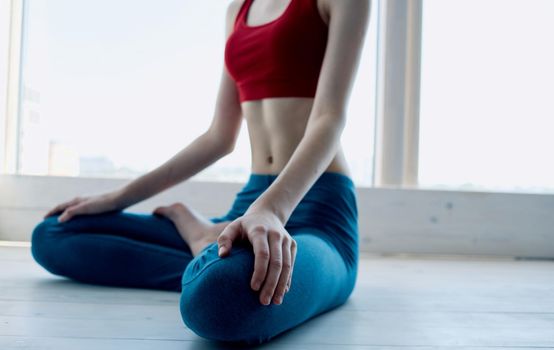 A woman is meditating near the window with her legs crossed and gesturing with her hands. High quality photo