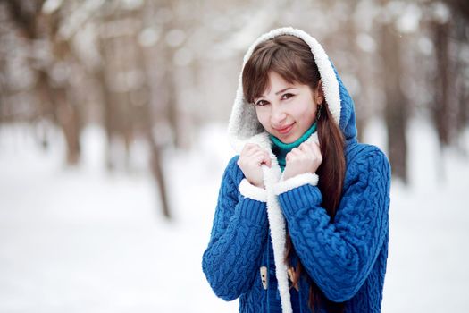 Winter portrait of a lovely girl in a blue sweater on the background of a snowy forest.