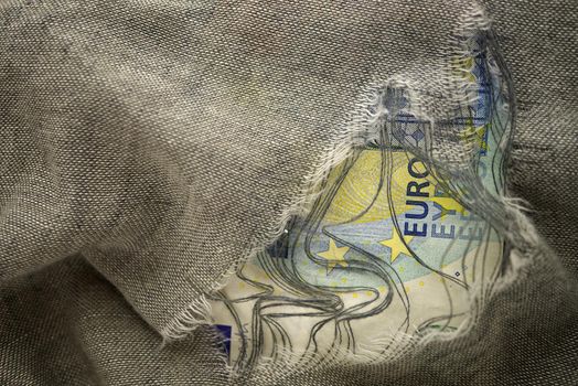 Euro bill viewed through a hole in torn grey fabric in a budget hole or economic concept
