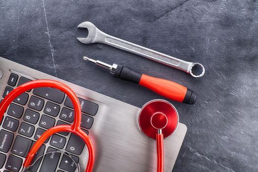 Computer repair or maintenance concept with a stethoscope to check the status or health of the device on top of a laptop with screwdriver and spanner