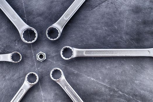 Spanners or wrenches arranged around the nut an grunge stone surface, top view