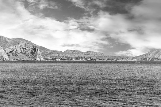 Black white photo. Mountains of the sea and a boat. On the horizon resort buildings.