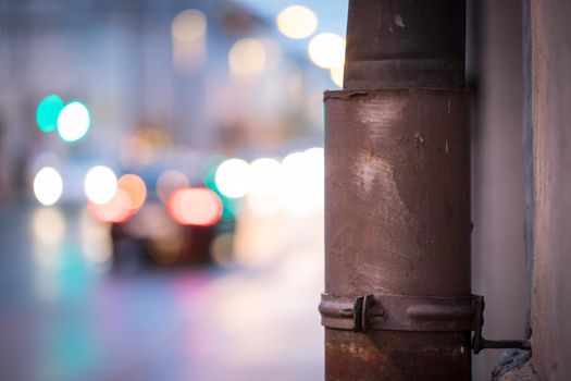 Closeup of rain drain, urban city lights in the blurry background