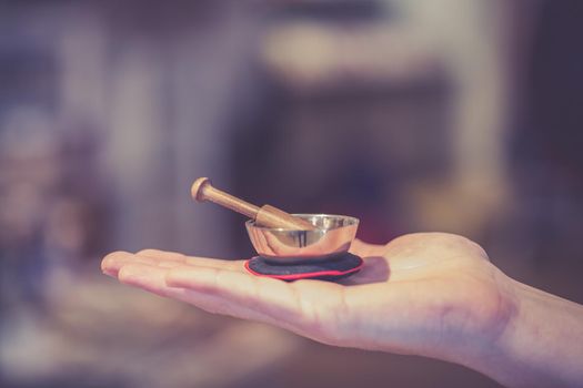 Small singing bowl holding in hand, blurry background