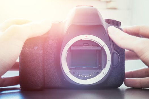 Hands of a photographer are touching a professional reflex camera, open sensor. Sunlight.