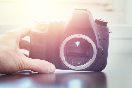 Hands of a photographer are touching a professional reflex camera, open sensor. Sunlight.
