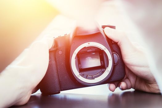 Hands of a photographer are touching a professional reflex camera, open sensor. Sunlight.
