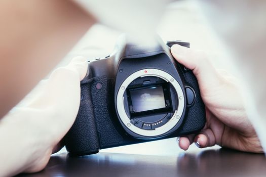 Hands of a photographer are touching a professional reflex camera, open sensor