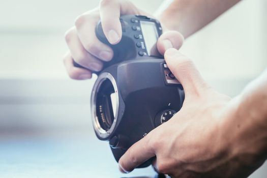 Hands of a photographer are touching a professional reflex camera, open sensor