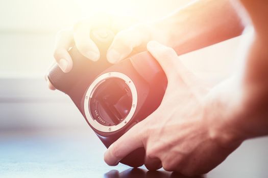 Hands of a photographer are touching a professional reflex camera, open sensor. Sunlight.