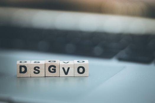 Wooden cubes with the letters “DGSVO” for Datenschutzgrundverordnung are lying on a laptop