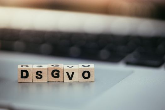 Wooden cubes with the letters “DGSVO” for Datenschutzgrundverordnung are lying on a laptop