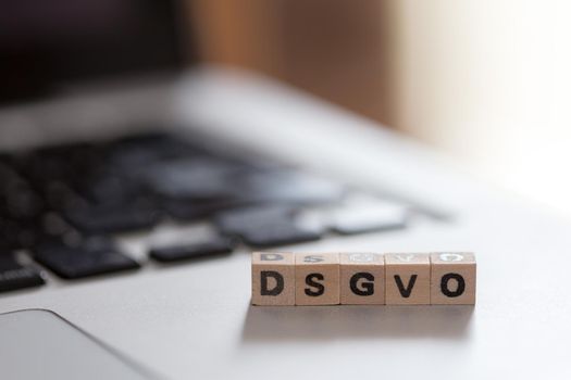 Wooden cubes with the letters “DGSVO” for Datenschutzgrundverordnung are lying on a laptop