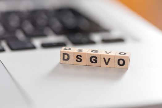 Wooden cubes with the letters “DGSVO” for Datenschutzgrundverordnung are lying on a laptop