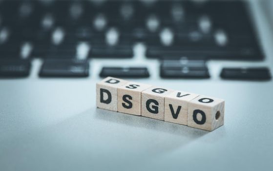 Wooden cubes with the letters “DGSVO” for Datenschutzgrundverordnung are lying on a laptop