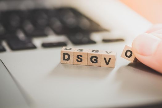 Wooden cubes with the letters “DGSVO” for Datenschutzgrundverordnung are lying on a laptop