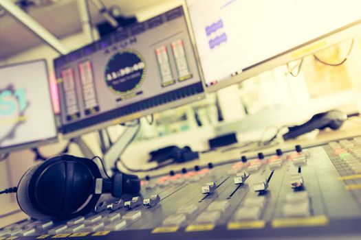 Close up picture of a soundboard in a broadcasting studio, computers in the blurry background