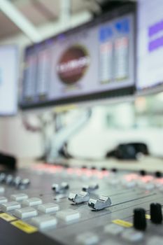 Close up picture of a soundboard in a broadcasting studio, computers in the blurry background