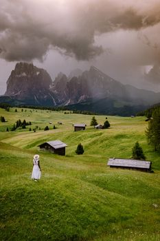 Alpe di Siusi - Seiser Alm with Sassolungo - Langkofel mountain group in background at sunset. Yellow spring flowers and wooden chalets in Dolomites, Trentino Alto Adige, South Tyrol, Italy, Europe. Summer weather with dark clouds rain, couple men and woman on vacation in the Dolomites Italy