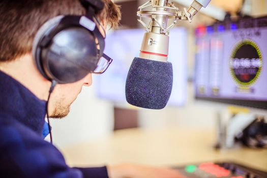 Young man in the broadcasting studio, radio, talking into the microphone