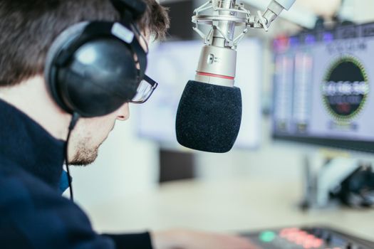 Young man in the broadcasting studio, radio, talking into the microphone