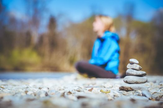 Cairn on a pebble beach, meditating woman in the background