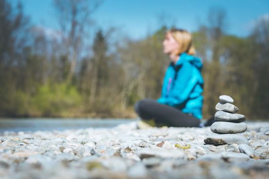 Cairn on a pebble beach, meditating woman in the background