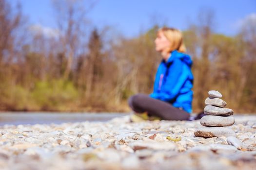 Cairn on a pebble beach, meditating woman in the background